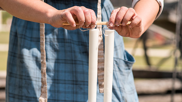 Gros plan d’un employé de Parcs Canada en tenue d’époque qui retire deux bougies blanches d’un moule à l’aide d’un bâton de bois.