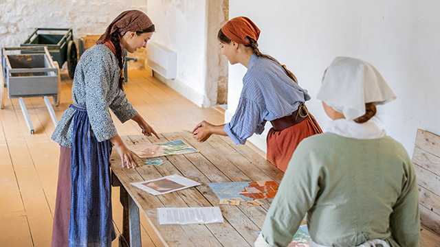 Trois employées de Parcs Canada en tenue d’époque font une activité à l’aide d’une carte et de fiches.