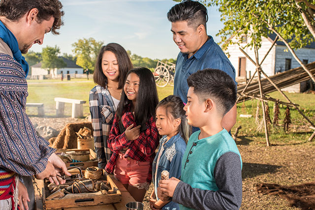 Un employé de Parcs Canada en tenue historique présente une exposition d’artefacts à un groupe de cinq visiteurs.