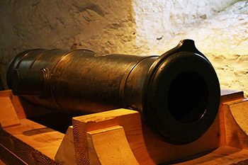 One of the cannon from York Factory supported in a wooden display case, from a three-quarter view. 
