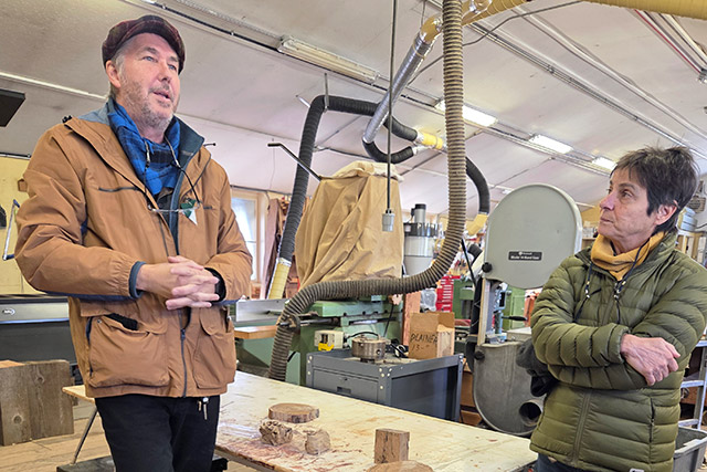 One person speaks while standing in a workshop at Lower Fort Garry as another person looks at him.