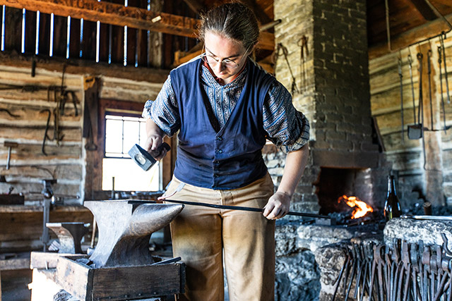 A blacksmith hammers a piece of metal on an anvil.