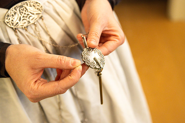 A close-up of a Parks Canada employee’s hands holding a metal tool attached by a chain to a chatelaine around her waist.