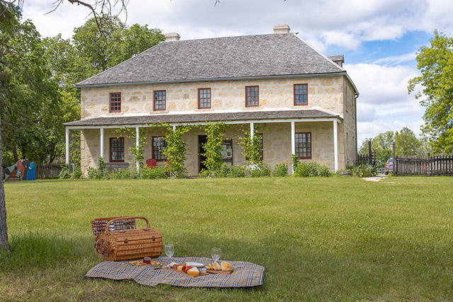 Plates of bread, cheese, crackers and meats and a picnic basket on a blanket in front of St. Andrew’s Rectory.