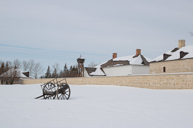 A Red River cart near the Tyndall Stone walls of Lower Fort Garry during the winter.