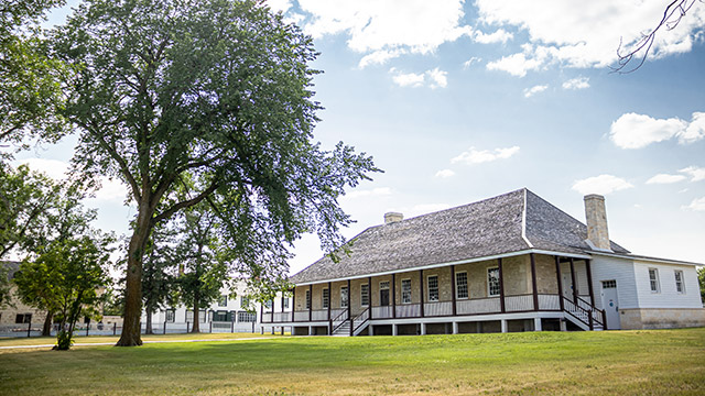 Historic buildings of Lower Fort Garry and the surrounding trees and lawn in the summertime.