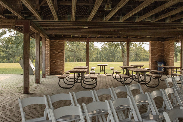 White chairs are arranged in rows with an aisle in the middle under the picnic structure at Lower Fort Garry National Historic Site.