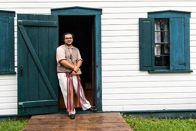 A person in historic clothing stands in front of a doorway at Riel House.