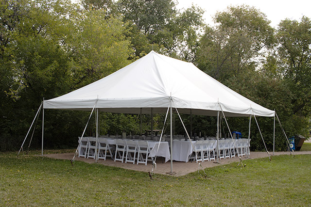 Chairs are seen arranged around rectangular tables under a tent at Riel House National Historic Site.