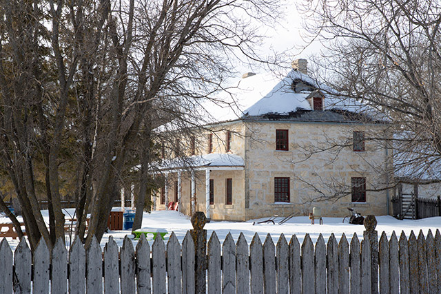 A two-story limestone building seen from the side during winter.