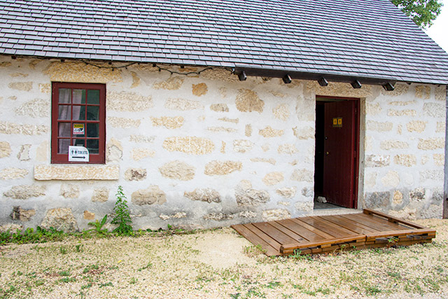 A wooden boardwalk leading from a gravel lot into a stone building.