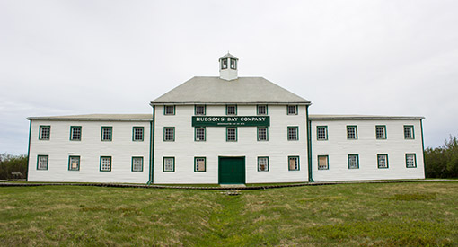 A large white building with three distinct sections: a three-storey section in the middle and two-storey sections on either side. A sign in the centre above the second-floor windows says “Hudson’s Bay Company”.