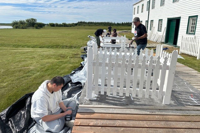 People assemble small white fences on a boardwalk.