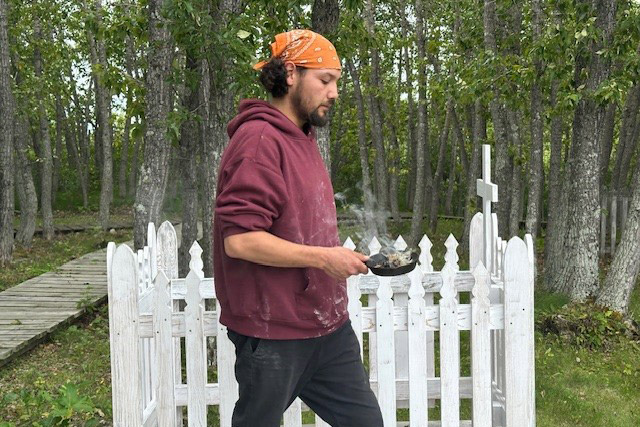A person holds a small cast-iron pan in front of a white fence surrounding a grave.