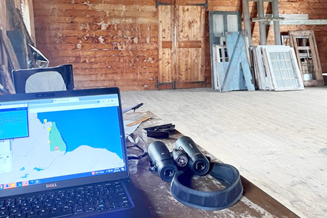A laptop and binoculars on a well-worn table inside the York Factory depot building.