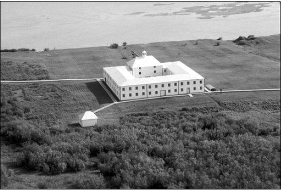 An aerial view of a large white building. A river is seen at the top of the image.
