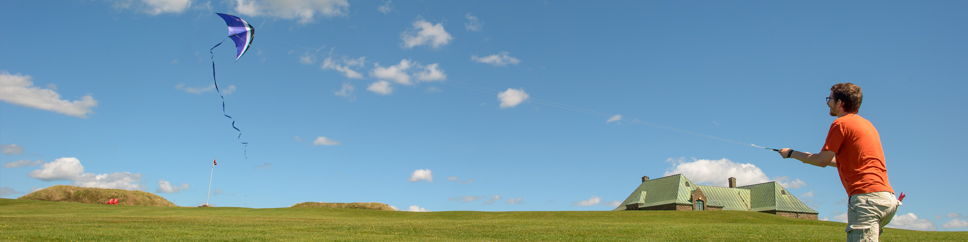 A man flies a kit in a vast open area, with the Fort and the visitor centre in the background.