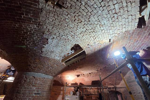 Workers restore a brick pillar holding up a vaulted brick ceiling.