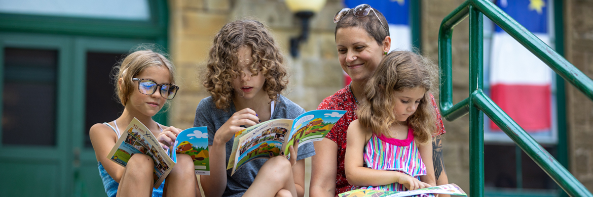 A mother and her children looking at the Xplorers booklet on the stairs in front of Monument-Lefevbre National Historic Site