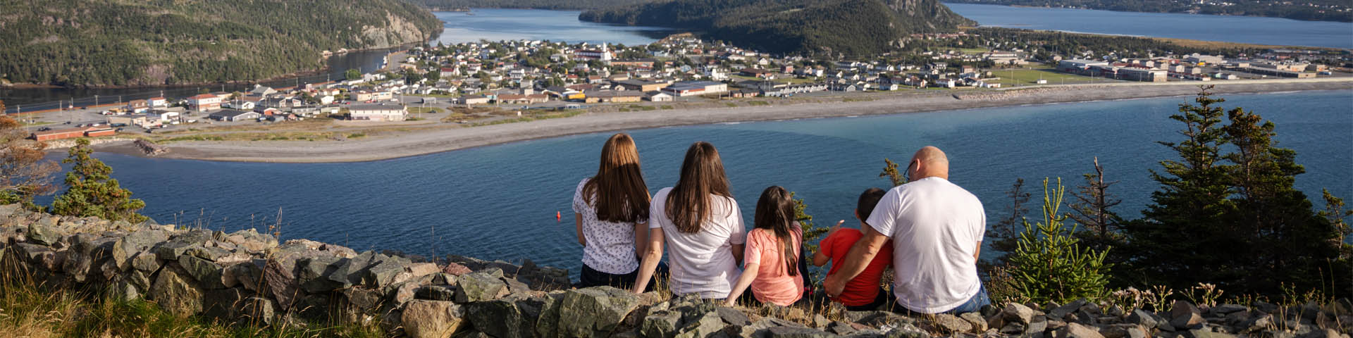 une famille de cinq personnes assise sur un mur de pierre surplombant une ville au bord de l'océan