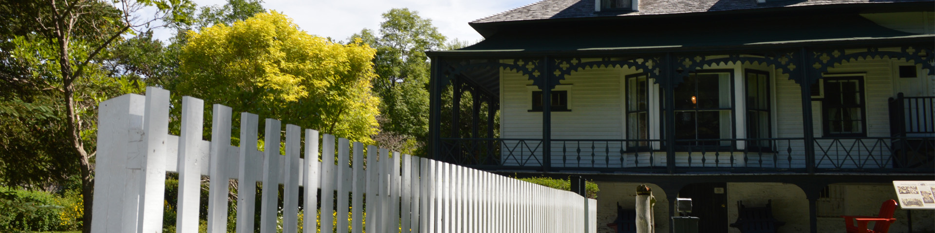 close-up of a white fence leading to a white cottage with a green veranda