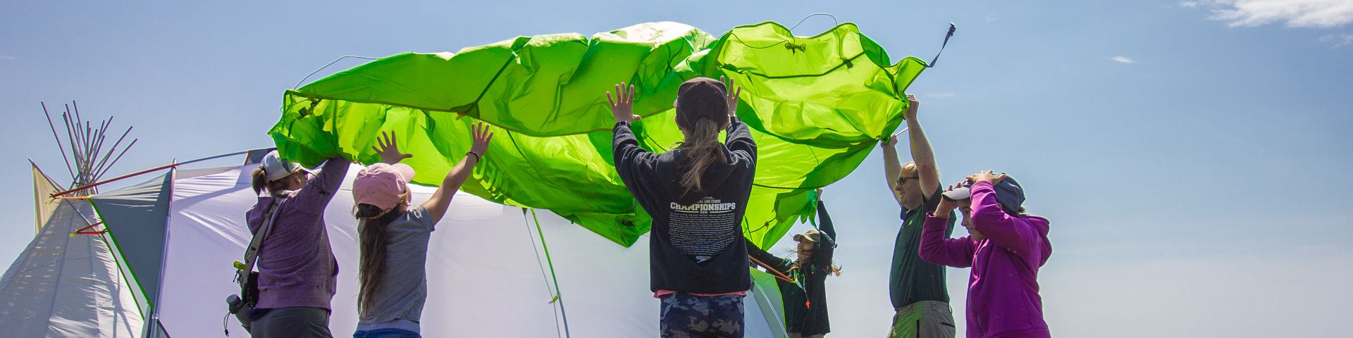 A person in Parks Canada uniform sets up a tent with a group of young visitors at Port au Choix National Historic Site