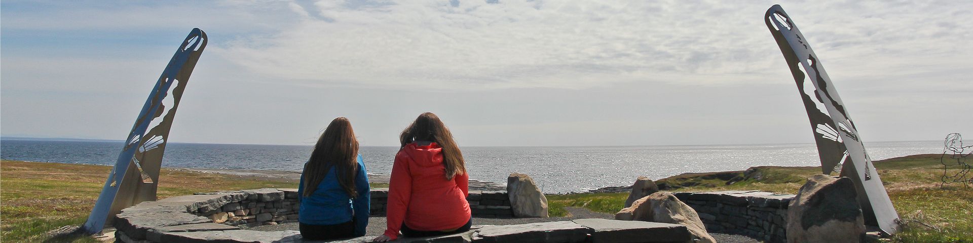 Deux personnes sont assises sur un banc de pierre circulaire et regardent vers la côte au lieu historique national de Port au Choix