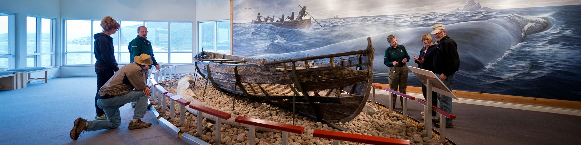 Parks Canada staff talk to a group of visitors next to a display of a Basque boat at Red Bay National Historic Site