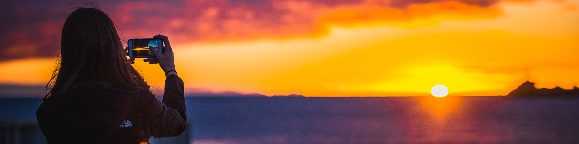 un individu prenant une photo du coucher de soleil avec son téléphone portable. 