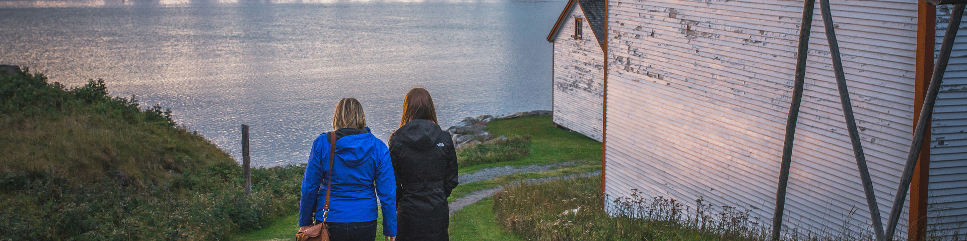 two individuals walking on a grassy path towards the water