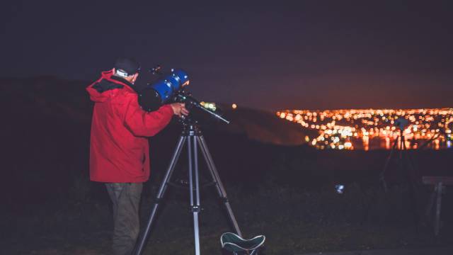 Une personne regardant dans un télescope dans l'obscurité, avec la ville illuminée en arrière-plan.
