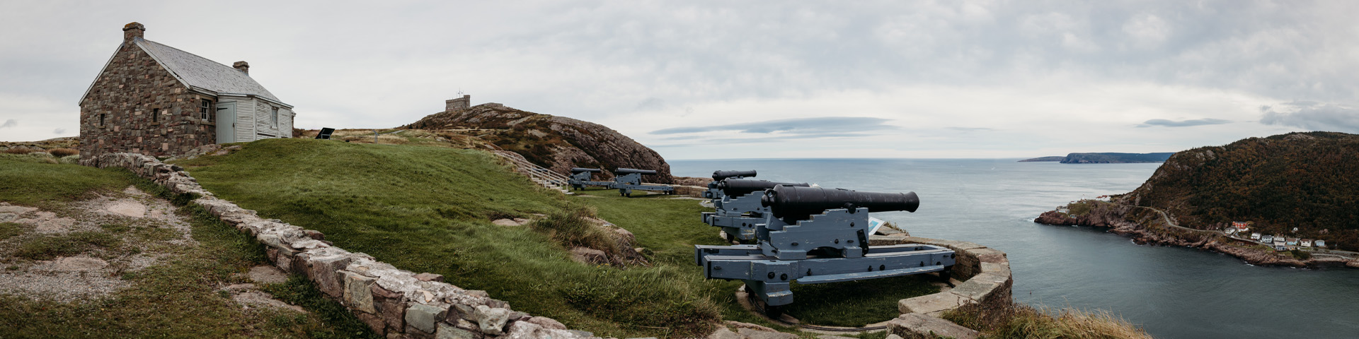 a coastal hill with historic cannons and two stone buildings. 