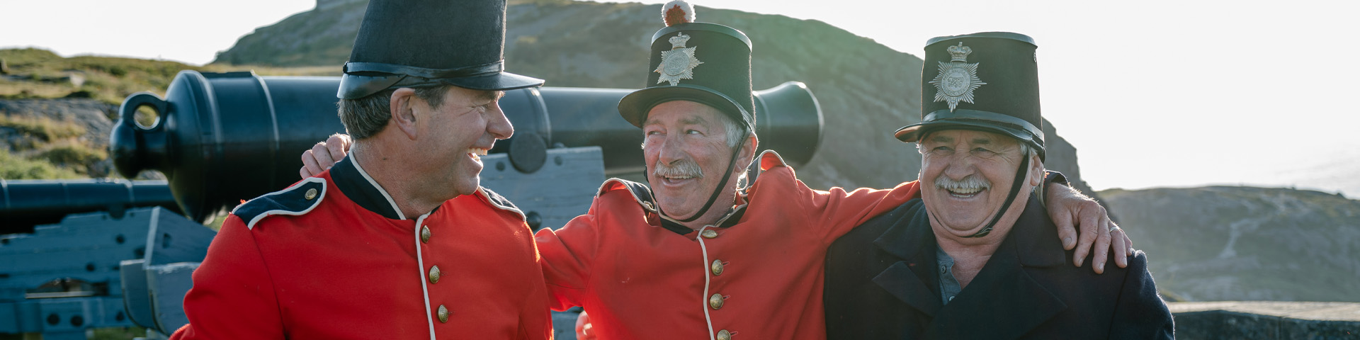 three individuals in historic military costume laughing with their arms around each other