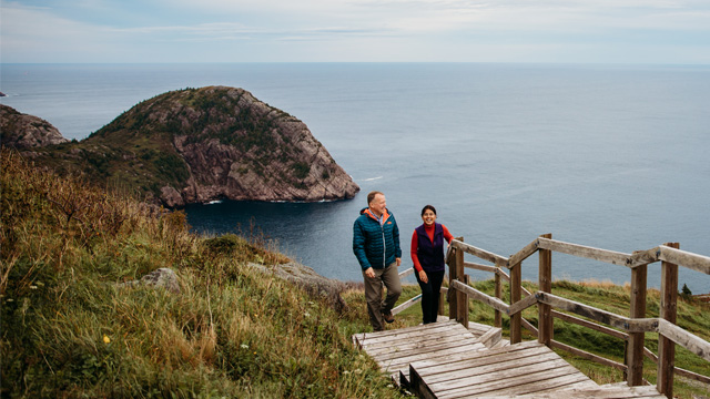 two people walking on wooden stairs overlooking the ocean.