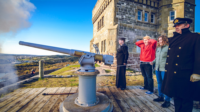 two visitors firing a large cannon, with two Parks Canada employees in historic uniform
