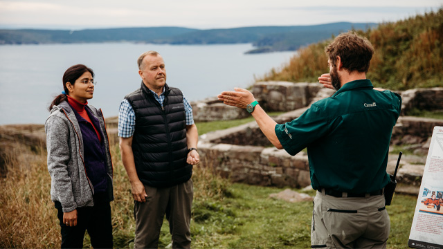 a Parks Canada employee giving a theatrical tour to two people on a coastal hill 