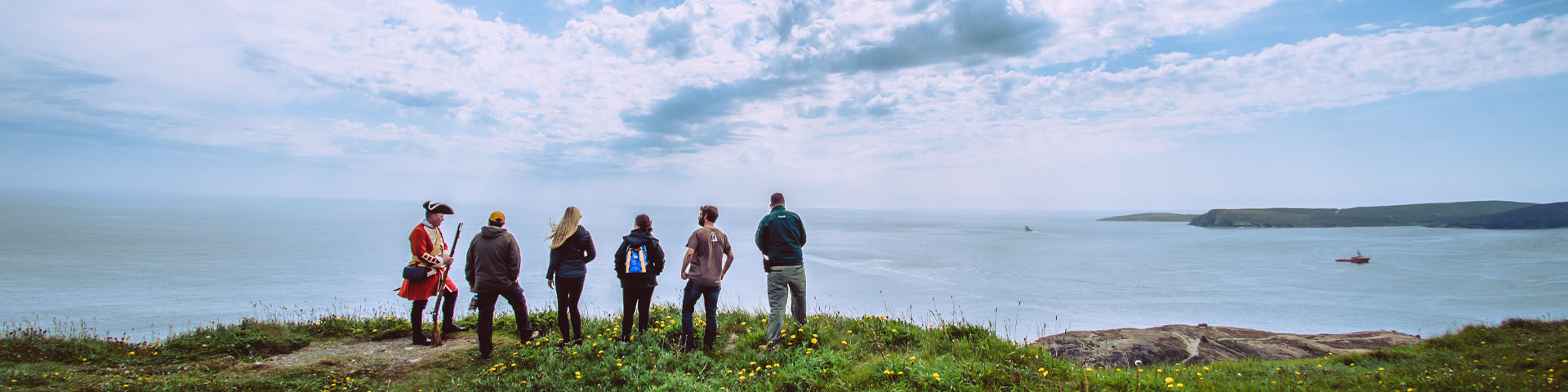 a group of 6 people standing on a coastal edge, overlooking the ocean