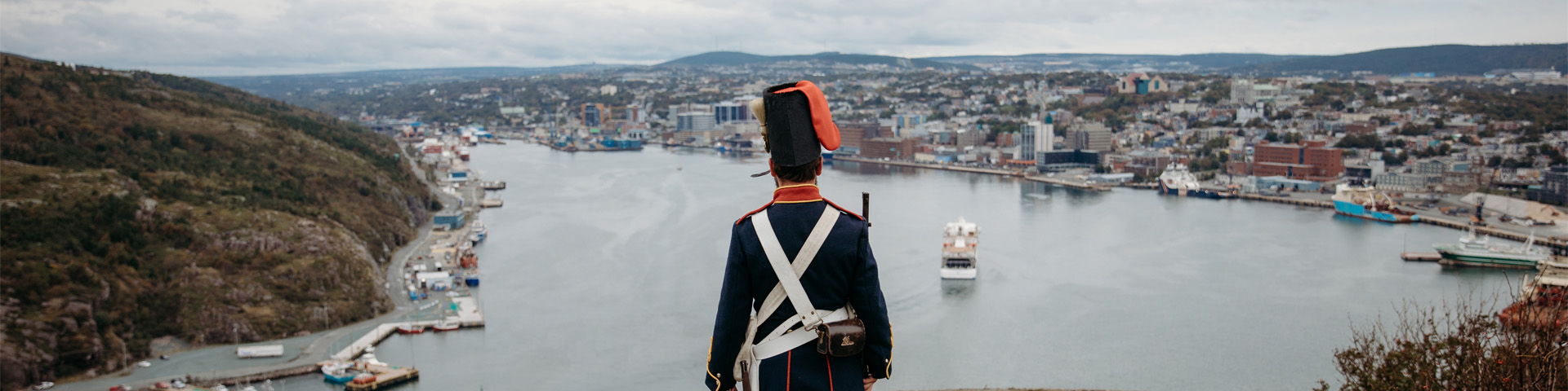 un homme en uniforme militaire historique, surplombant le port d'une ville.