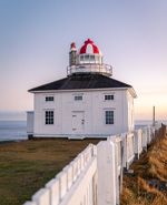 a square, white lighthouse on a coastal cliff
