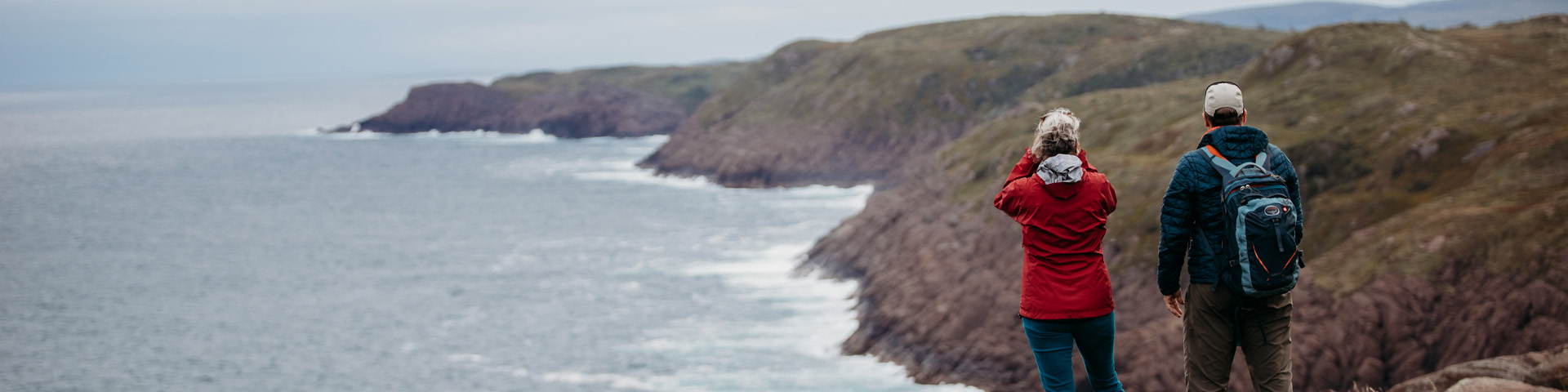 two people standing on a cliff-top path overlooking a coastal trail