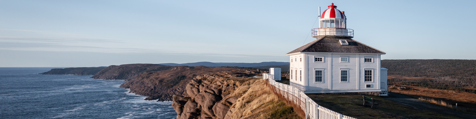 a square, white and red lighthouse on the edge of an oceanside cliff