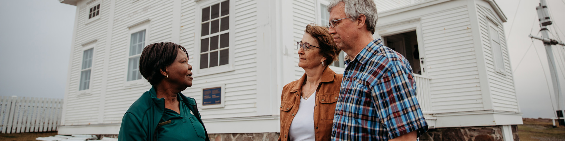 a Parks Canada employee talking to two people outside of a white clapboard building