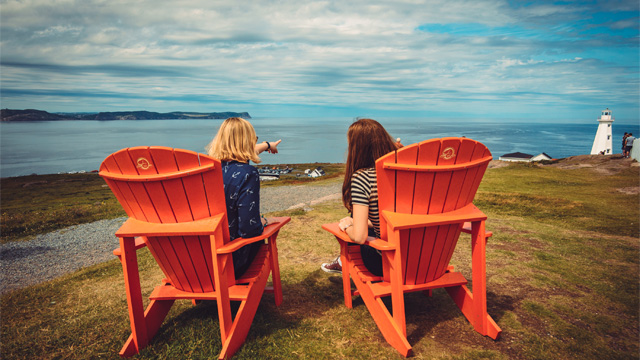 two people sitting in red Adirondack chairs watching and pointing at the ocean