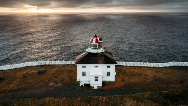 a white and red building on a grassy, coastal cliff