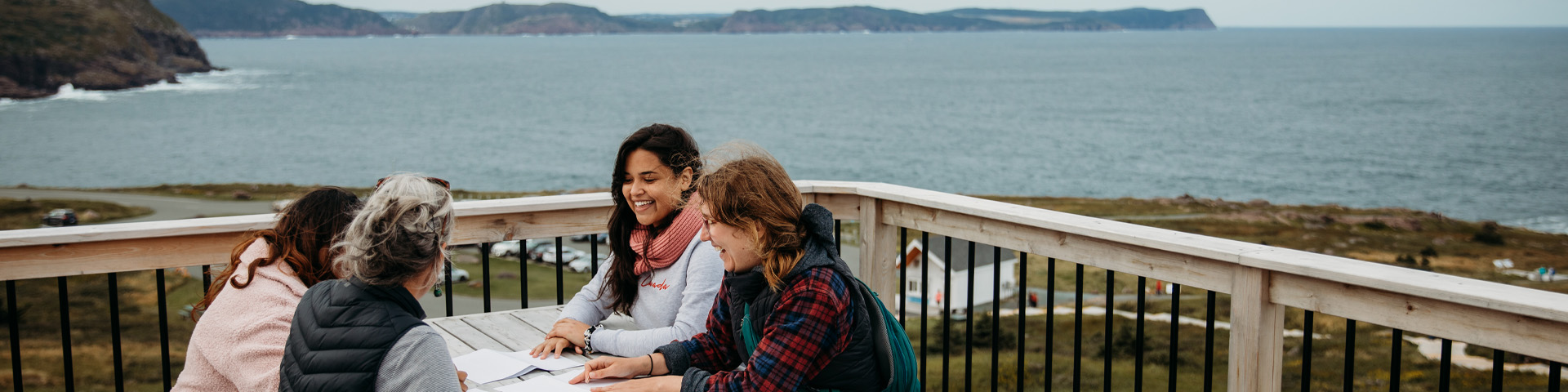 Four individuals laughing at a picnic table overlooking the ocean.
