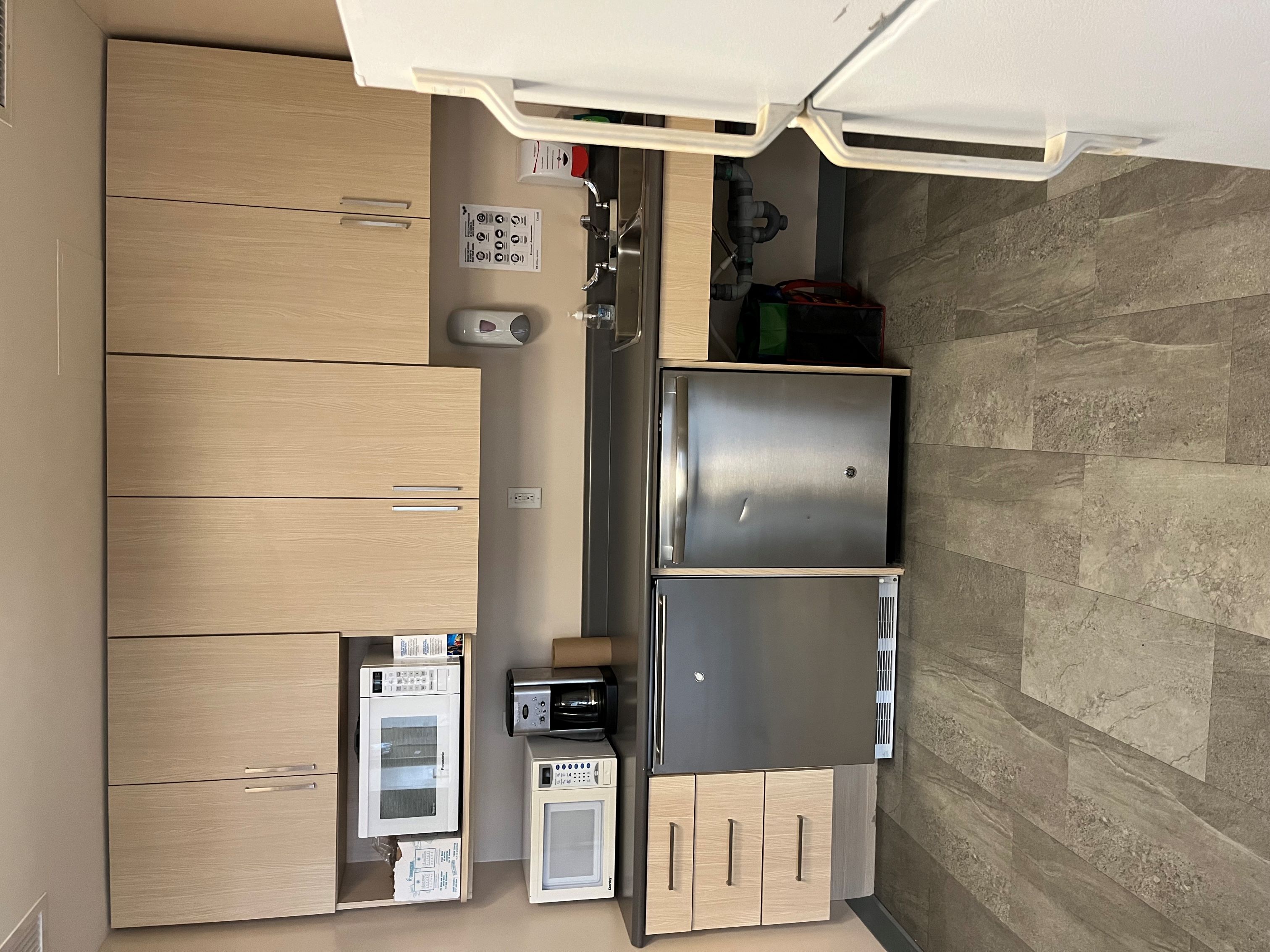 A kitchenette with cabinets, two microwaves, a double sink, 2 dishwashers, and a full sized fridge with a freezer.