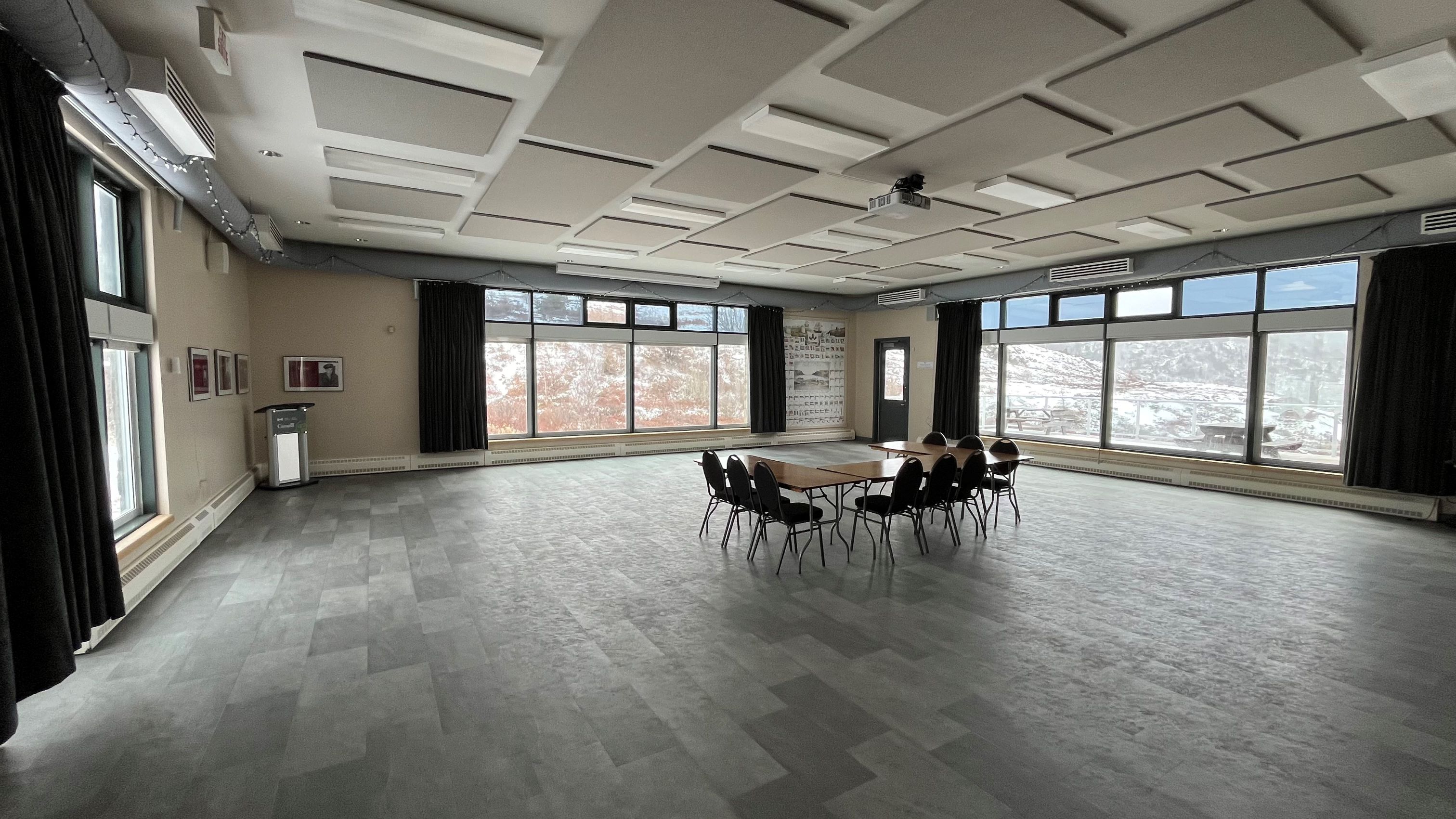 An event room with two window that have open curtains and chairs surrounding a table in the middle of the room.