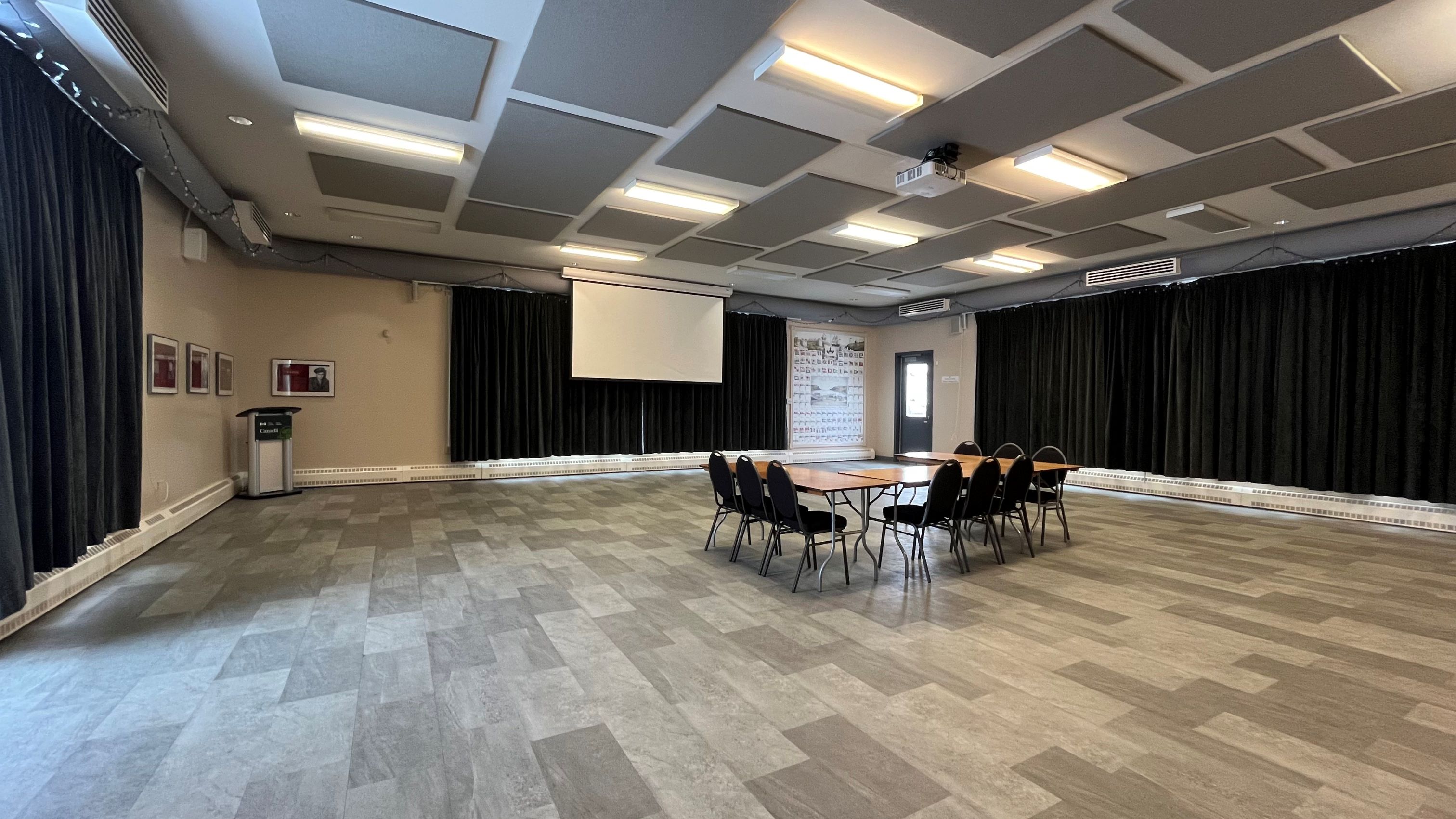 An event room with chairs surrounding a table in the middle of the room, two closed curtains, and a projector lowered from the ceiling.