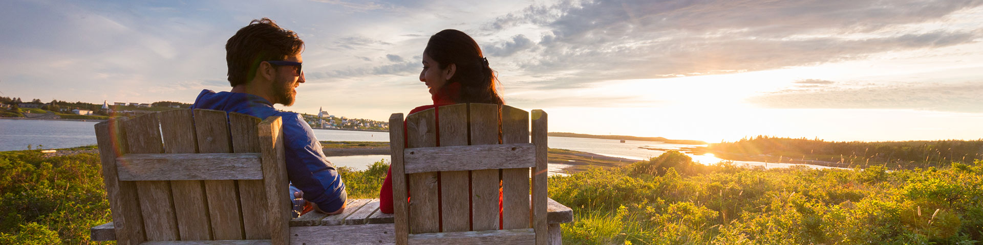 Two people sit in wooden chairs while the sunsets in front of them
