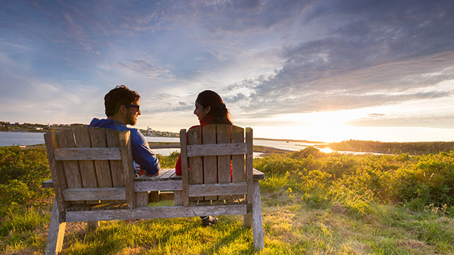  A man and a woman sitting in wooden chairs while the sunsets